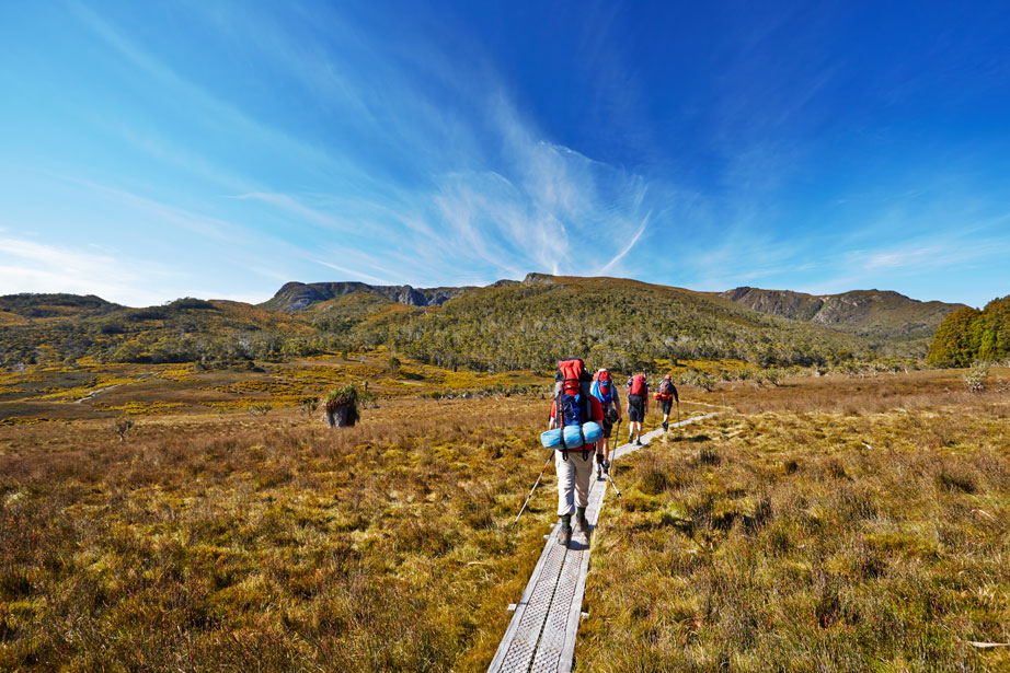 People with backpacks hiking on a path towards a small mountain